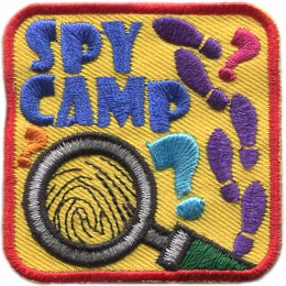 A magnifying glass magnifies a fingerprint. The words Spy Camp are above it, and the right side has shoe prints.