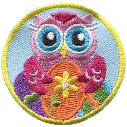 A pink owl holds a painted Easter egg decorated with a flower. Two other painted eggs sit in the background of this round crest.
