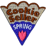 The words Cookie Seller Spring are on a cookie slice with blue icing and a pink flower.