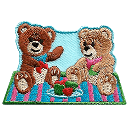 Two teddy bears sit on a picnic blanket eating red and green apples on a clear day.