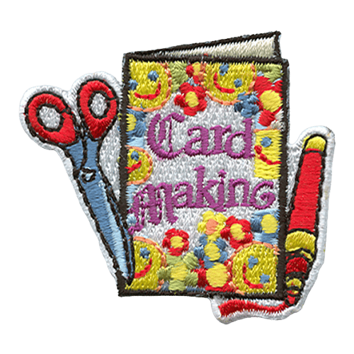 A flower and smiley face decorated card is displayed with the words ''Card Making'' on it. A marker lays next to the card on the right and scissors slightly lay on top of the card to the left.