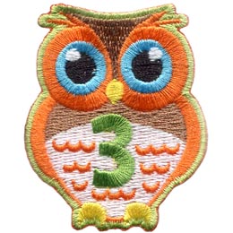 An orange owl with big blue eyes stands at the ready. The number 3 is embroidered in green on the owl's chest.