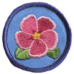 This merrow bordered circle badge has a pink primrose in the center with two green leaves peeking out.