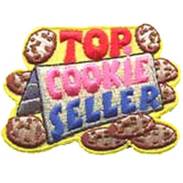 A folded piece of paper displays the words ''Cookie Seller.'' Above the sign the word ''Top'' is surrounded by a cookie on either side. Other cookies lay scattered around the sign.