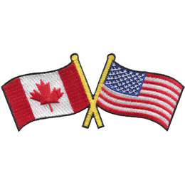 This badge displays the Canadian flag on the left and the United States flag on the right. The flag poles of each flag are crossed with each other, forming a X shape.
