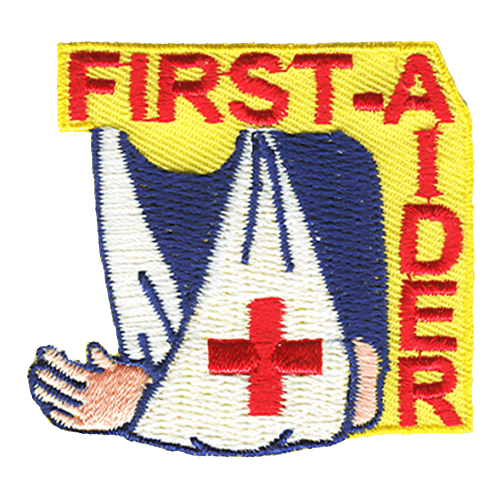 A person's shoulders and arm are visible in this yellowed background patch. The person's arm is in a white sling with a red cross displayed on the front. The word First-Aider is displayed in a backwards and upside down L shape running along the top and down the right hand side of the crest.