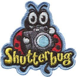 A ladybug holds a camera as if it is about to snap a photo. The word 'Shutterbug' is embroidered under the camera, but overlapping the ladybug's legs.