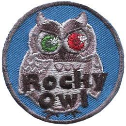 This grey owl looks like a statue with one ruby and one emerald eye. Text near the bottom of the crest says \'Rocky Owl\'.