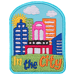 A sunny cityscape sits on top of a green hill. The words In The City are embroidered below.