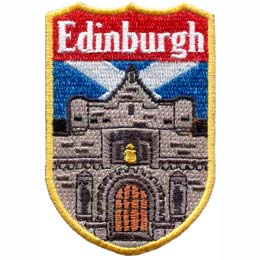 An embroidered image of a castle dominates this shield shaped patch. The word Edinburgh sits at the top of the emblem. The blue and white crossed Scottish flag is pictured in the background.