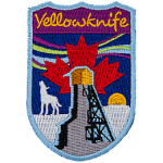 The name Yellowknife is above the northern lights and a howling wolf. A red maple leaf is in the middle of the sky.