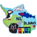 This crest is shaped like the province of Newfoundland and Labrador. Decorating it are the initials NL, a cod with a red kiss mark on it, a dog, a puffin, the ocean, and the capital city St. John's.