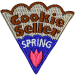 The words Cookie Seller Spring are on a cookie slice with blue icing and a pink flower.