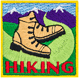 Two hiking boots on a trail that leads into the mountains. The word Hiking is stitched below.